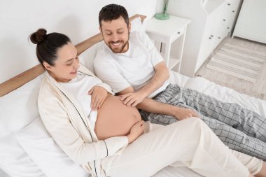 Mutlu hamile çift yatak odasında yatıyor.