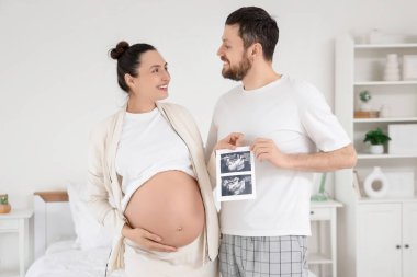 Yatak odasında ultrason görüntüsü olan mutlu hamile çift.