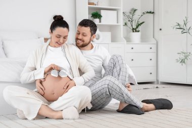 Bebek poposu olan mutlu hamile çift yatak odasında oturuyor.