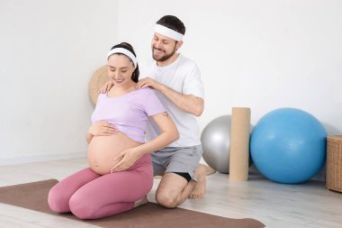 Sportif genç adam spor salonunda hamile karısının omuzlarına masaj yapıyor.