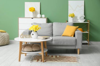 Soyunma odası, kahve masası ve yeşil duvarlı narsist çiçekli rahat bir kanepe.