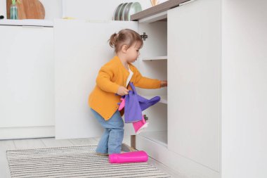 Sevimli küçük kız mutfaktaki açık çekmeceden lastik eldiven alıyor. Tehlikedeki çocuk