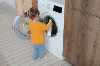 Evde çamaşır makinesine çamaşır deterjanı koyan tatlı küçük bir kız. Çocuk tehlikede.