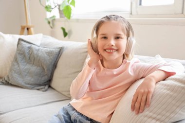 Kulaklıklı küçük kız evdeki kanepede oturuyor.