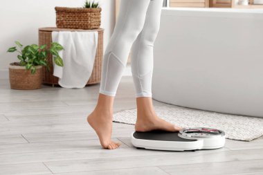 Spor bacaklı bir kadın banyoda tartıyla ağırlığını ölçüyor.