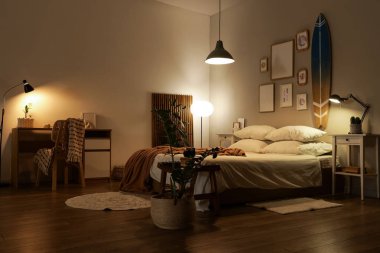 Geceleri karanlık yatak odasının içinde sörf tahtası, masa ve parlayan lambalar var.