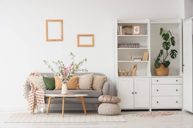 İçinde vazo, kanepe ve dolapta çiçek açan dallarla aydınlık oturma odasının içinde.