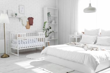 Yatak, beşik ve bebek kıyafetleriyle aydınlatma odasının içinde.