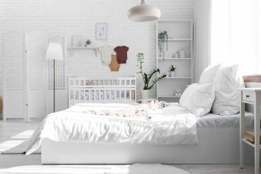 Yatak, beşik ve bebek kıyafetleriyle aydınlatma odasının içinde.