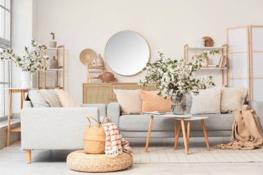 Kanepeleri ve vazolarında çiçek açan dalları olan aydınlık oturma odasının içinde.