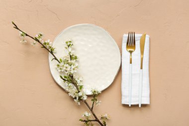 Altın çatal bıçak takımı ve bej arka planda çiçek açan dallı güzel bir masa.