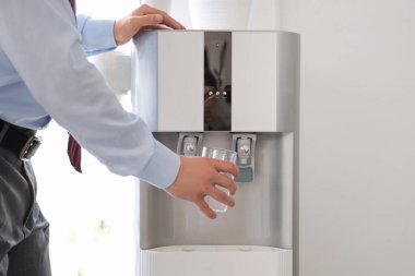 Genç işadamı ofisteki soğutucudan su dolduruyor