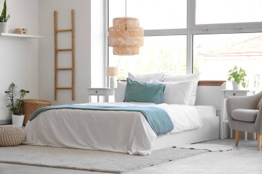 Büyük pencerenin yanında rahat yatağı ve gri koltuğu olan aydınlık yatak odasının içi.