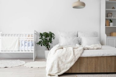 Yatak, bebek beşiği ve bitkisi olan ışık odasının içinde.