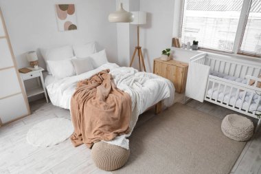 Büyük yataklı, bebek karyolası ve pencereli aydınlatma odasının içi.