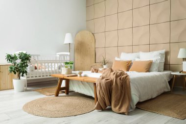 Büyük yataklı, bebek karyolası ve banklı şık bir oda.