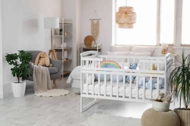 Bebek beşiği, raf üniteleri ve oyuncaklarla aydınlık yatak odasının içinde.