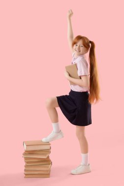 Pembe arka planda yığınla kitabı olan kızıl saçlı tatlı bir kız.