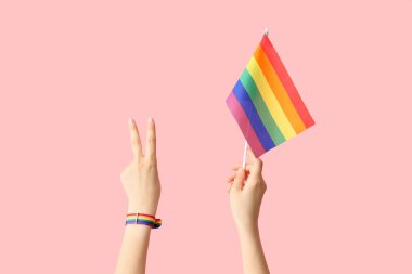 Pembe arka planda zafer jesti gösteren LGBT bayrağı taşıyan kadın eller
