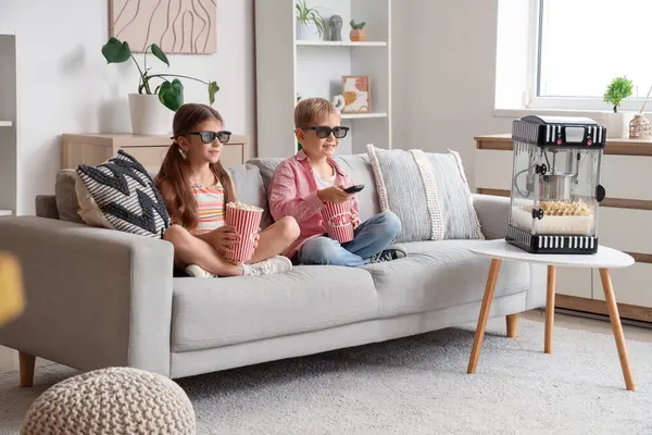 Üç boyutlu gözlüklü, patlamış mısırlı küçük çocuklar evde televizyon seyrediyor.