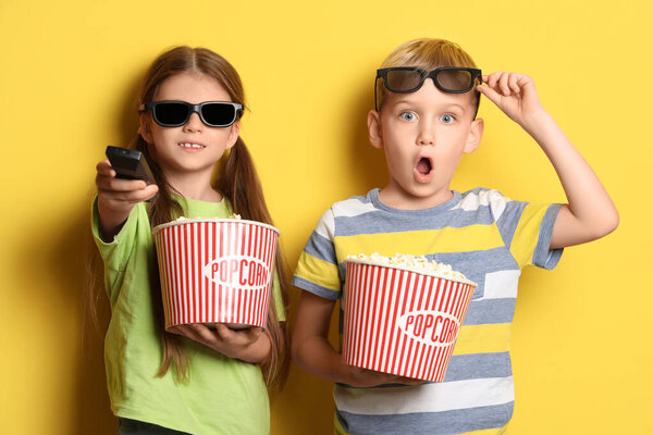 Little children in 3D glasses with popcorn watching TV on yellow background