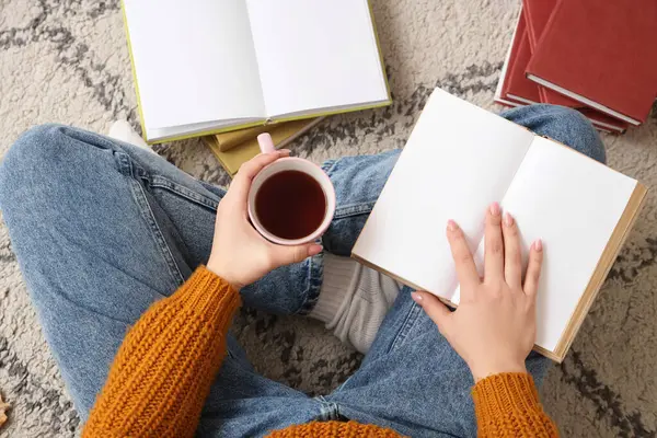Kahve fincanı ve boş kitapları olan kadın halıda oturuyor.