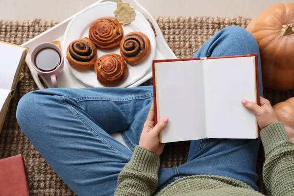 Boş kitapları ve çörekleri olan bir kadın halının üstünde oturuyor.