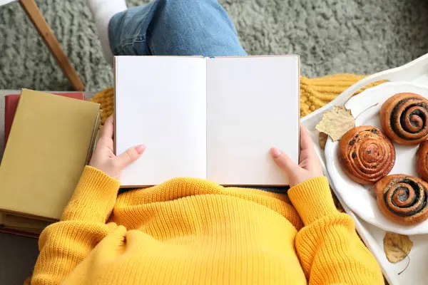 Evdeki kanepede kitap okuyan bir kadın.