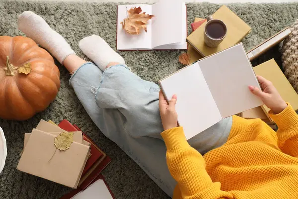 Kabaklı kitap okuyan kadın ve halıda sonbahar yaprakları, üst manzara.