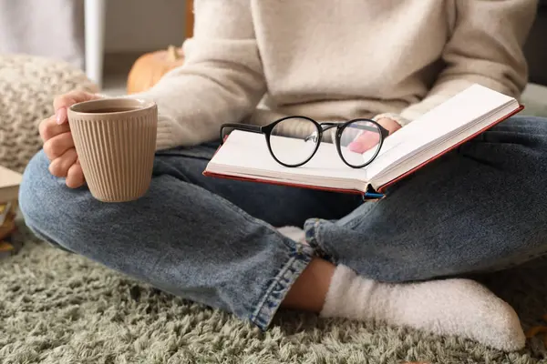 Kitaplı, gözlüklü ve kahve fincanı olan kadın evde oturuyor, yakın plan.