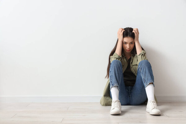Portrait of worried young woman sitting near light wall