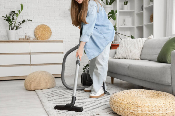 Young woman vacuum cleaning carpet in living room