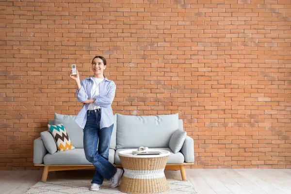 Duvarın yanında klimalı uzaktan kumandalı genç bir kadın.