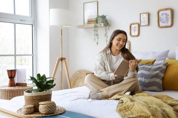 Молодая женщина читает книгу с доской для серфинга на скамейке в спальне