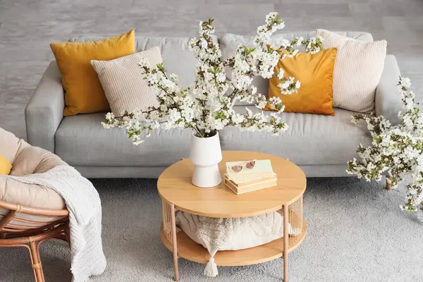 Oturma odasında çiçek açan dalları, güneş gözlükleri ve kitapları olan bir vazo.