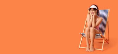 Güzel Afro-Amerikalı kadın, mayolu güverte sandalyesinde oturuyor, turuncu arka planda mesaj için yer var.