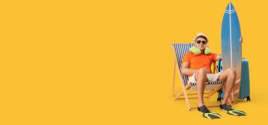 Güverte sandalyesinde oturan sörf tahtası olan genç erkek turist sarı arka planda mesaj için yer var.