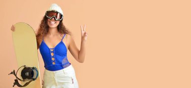 Kadın Afro-Amerikalı snowboardcu bej arka planda zafer jesti gösteriyor.