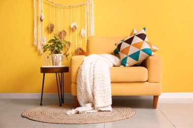 Sarı duvarın yanındaki sehpanın üzerinde ekoseli ve çiçekli rahat bir koltuk.