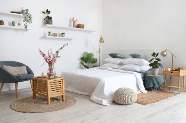 Şık bir yatak odasının içi. Ağaç dalları, ahşap bir masanın üstünde vazoda.