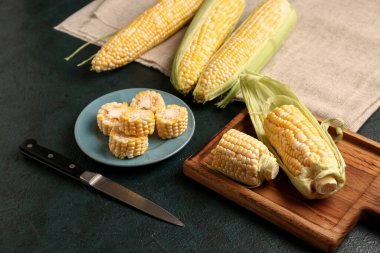 Siyah arka planda kesilmiş taze mısır koçanları olan tabak ve yemek.