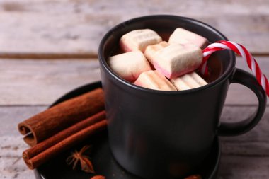 Bir fincan kremalı sıcak çikolata, şeker kamışı ve gri ahşap arka planda farklı baharatlar.