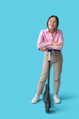 Mavi arka planda modern elektrikli scooterlı güzel bir Asyalı kadın.