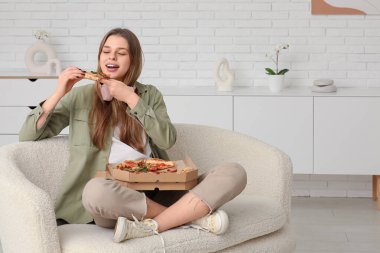 Genç kız oturma odasında lezzetli pizzalar yiyor.