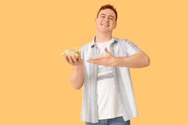 Genç adam gülümsüyor ve bej arka plandaki donör kebabına işaret ediyor.