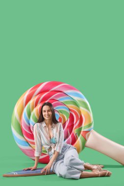 Yeşil arka planda oturan, sörf tahtası ve şişme yatağıyla gülümseyen genç kadın.