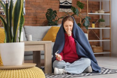 Hasta genç kadın battaniyeye sarılıp evde öksürüyor.