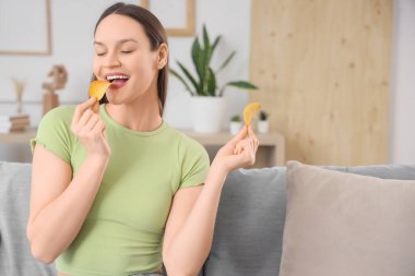 Evdeki koltukta patates cipsi yiyen genç bir kadın.