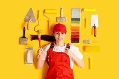 Sarı arka planda farklı malzemeler bulunan mutlu bir bayan dekoratör.