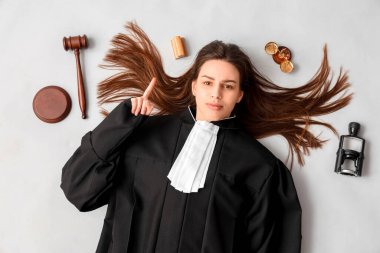 Elinde tokmak ve adalet terazisi olan genç bir kadın yargıç beyaz arka plandaki bir şeyi işaret ediyor.